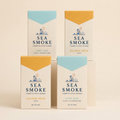 Four Sea Smoke packs on a cream studio backdrop — two Golden Hour, two Surf Wax
